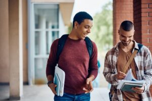 happy multiracial students reading from book while going to a class at the university