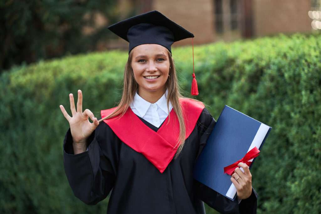 beautiful graduate girl graduation robe shows ok sign smiling camera